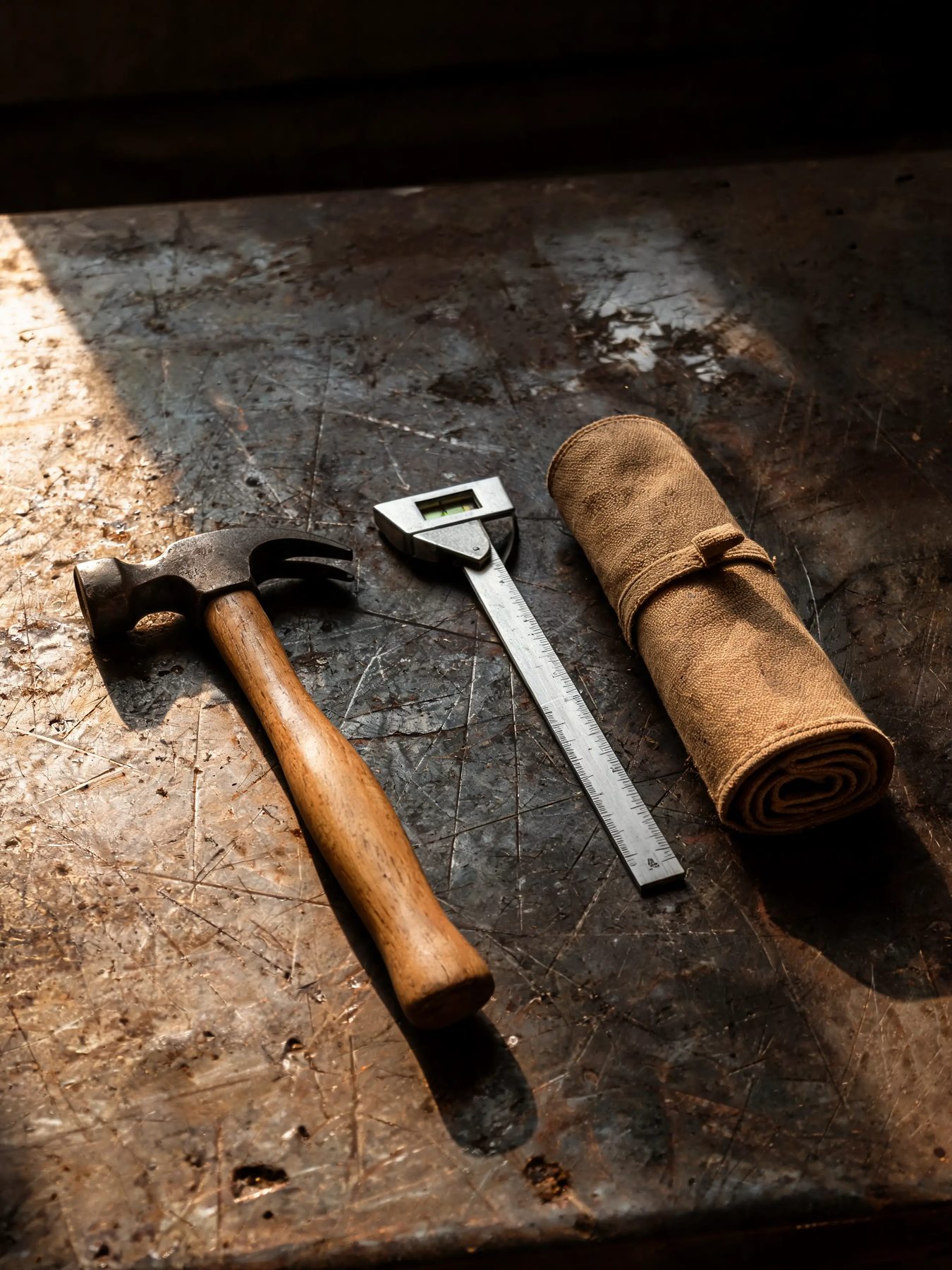 Hammer, combination square and canvas tool roll on a scarred steel bench